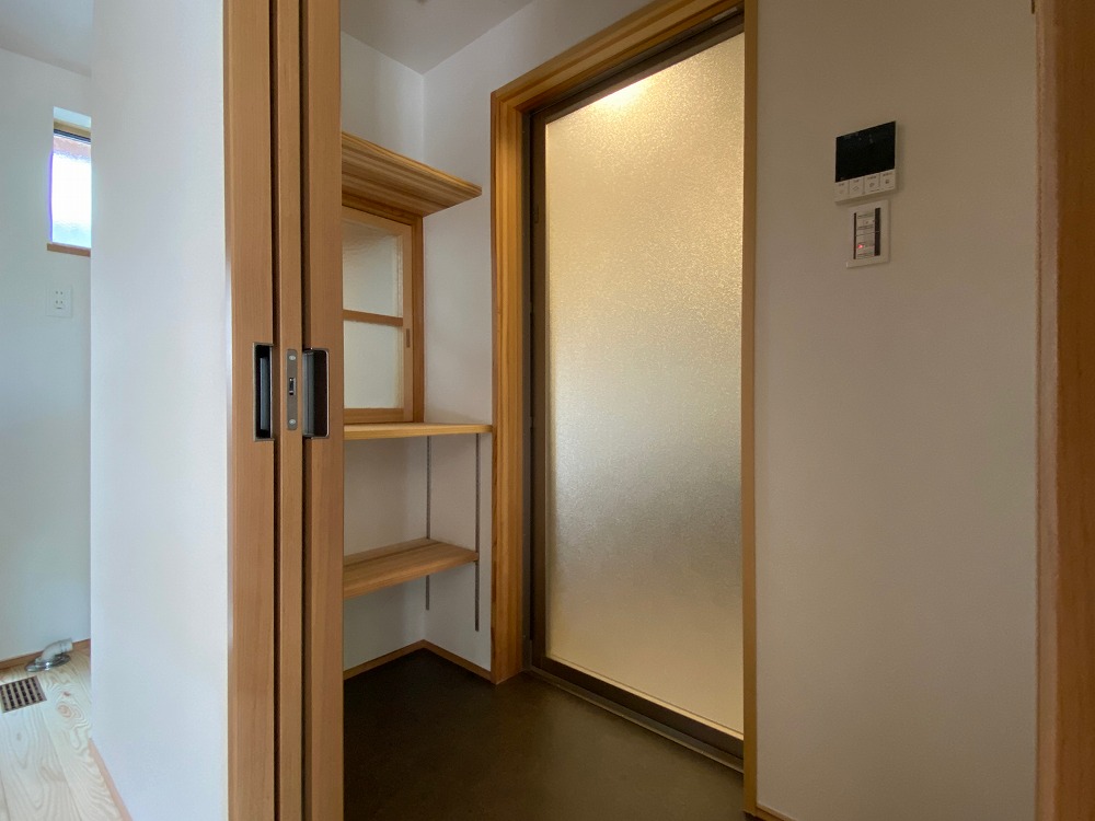 定番の小さなセパレート脱衣場。ちょっとした無垢の棚便利で、建具を開けると洗濯機にそのまま服を入れられる造りになっている